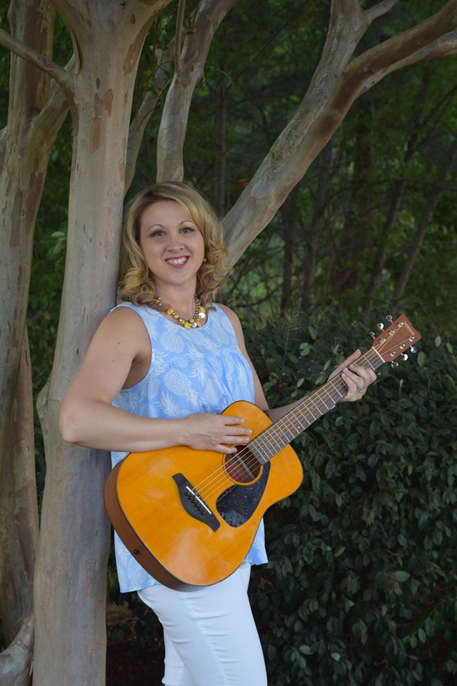 Laura Theismann holding an acoustic guitar outdoors